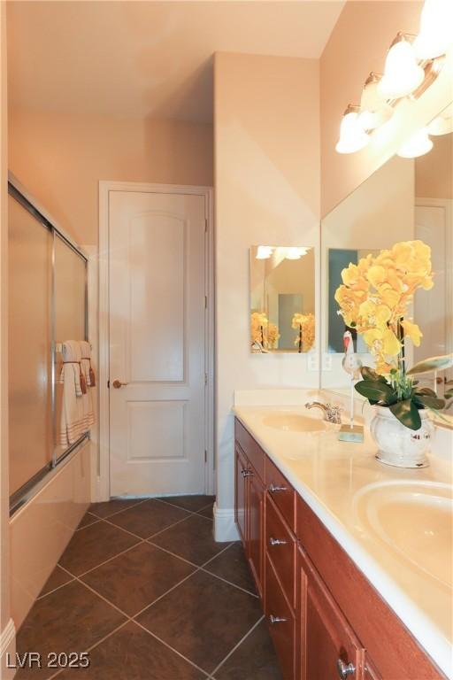 full bath with a sink, bath / shower combo with glass door, double vanity, and tile patterned floors