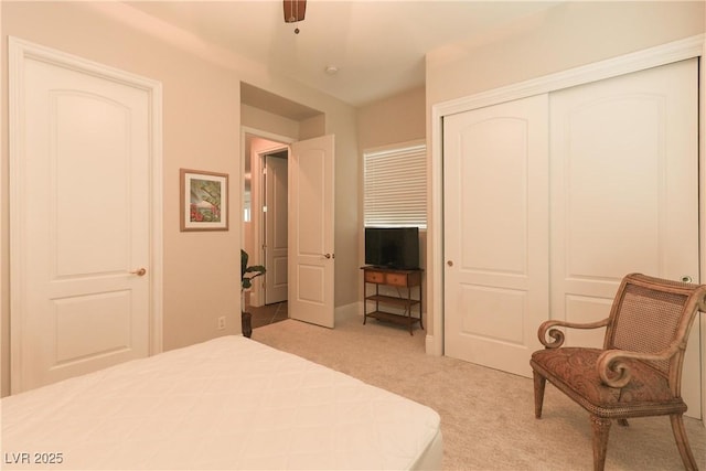 bedroom with a ceiling fan, a closet, and light carpet