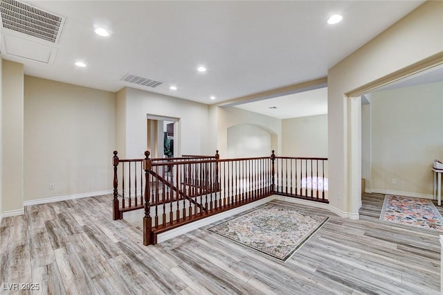 corridor with light wood-style flooring, an upstairs landing, and visible vents