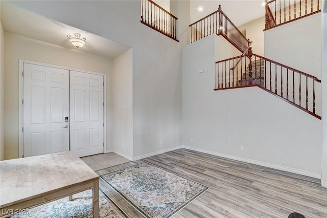 foyer entrance with a towering ceiling, stairs, baseboards, and wood finished floors