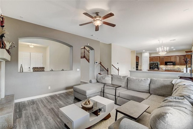 living room featuring baseboards, stairway, ceiling fan with notable chandelier, wood finished floors, and arched walkways