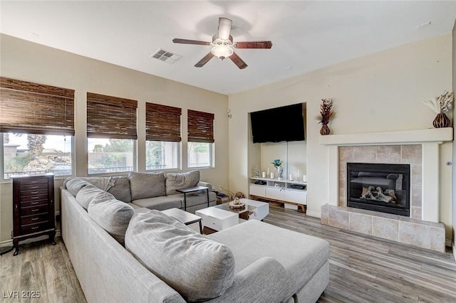 living room featuring a tiled fireplace, visible vents, light wood-style flooring, and ceiling fan