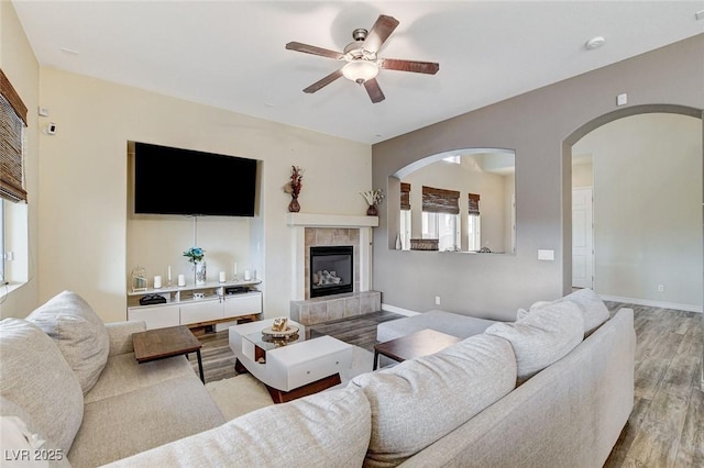 living area with a ceiling fan, wood finished floors, baseboards, and a tile fireplace