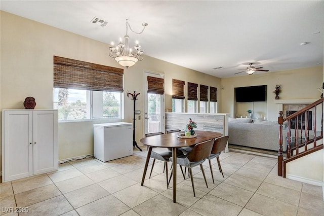 dining area featuring light tile patterned floors, visible vents, ceiling fan with notable chandelier, and stairway