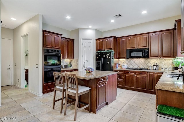 kitchen with light stone countertops, visible vents, a breakfast bar, black appliances, and a center island