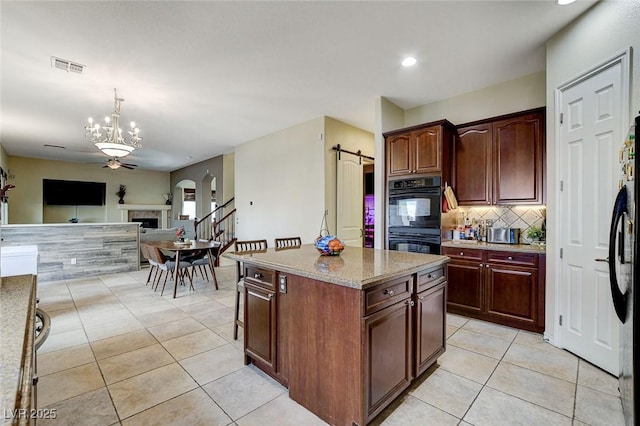 kitchen featuring open floor plan, a barn door, light tile patterned floors, decorative backsplash, and black appliances