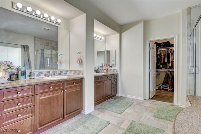 full bathroom with a walk in closet, a shower stall, two vanities, and a sink