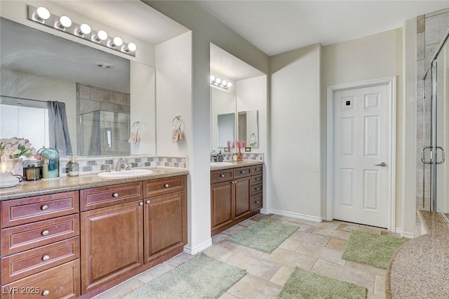 full bathroom featuring a shower stall, two vanities, baseboards, and a sink