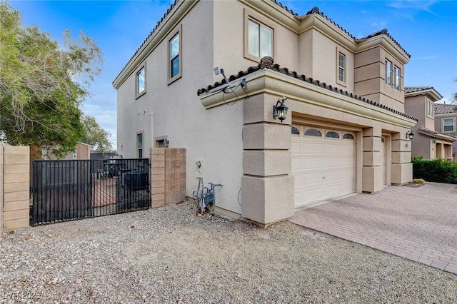 view of side of property featuring decorative driveway, fence, an attached garage, and stucco siding