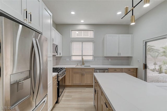 kitchen with tasteful backsplash, light wood-type flooring, appliances with stainless steel finishes, hanging light fixtures, and a sink