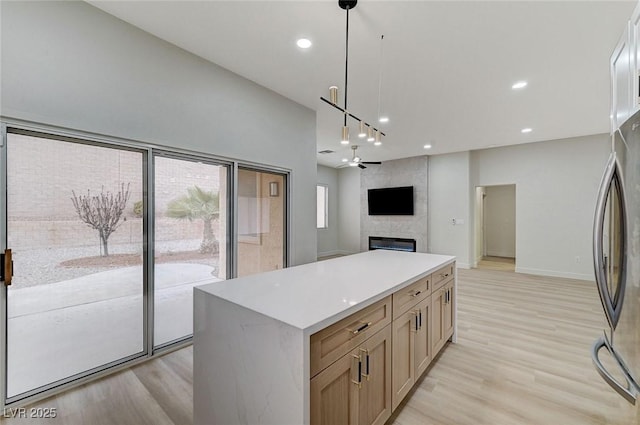 kitchen featuring a large fireplace, light wood-style flooring, a center island, and freestanding refrigerator