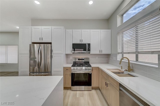 kitchen featuring a sink, light stone counters, tasteful backsplash, appliances with stainless steel finishes, and white cabinets