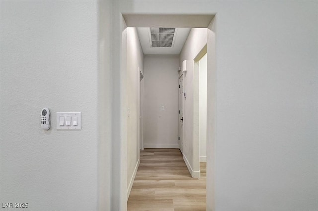 hallway with baseboards, visible vents, and light wood-type flooring