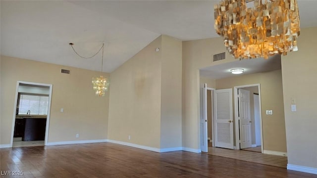 empty room featuring visible vents, wood finished floors, baseboards, and a chandelier