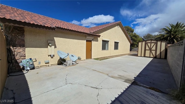 exterior space with stucco siding, a storage shed, an outdoor structure, and a tile roof