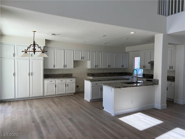 kitchen with visible vents, pendant lighting, dark stone countertops, light wood-style flooring, and a sink