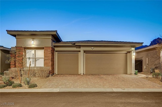 prairie-style house featuring decorative driveway, an attached garage, brick siding, and stucco siding