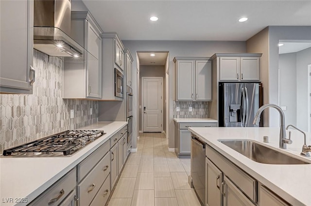 kitchen with gray cabinets, a sink, stainless steel appliances, light countertops, and wall chimney range hood