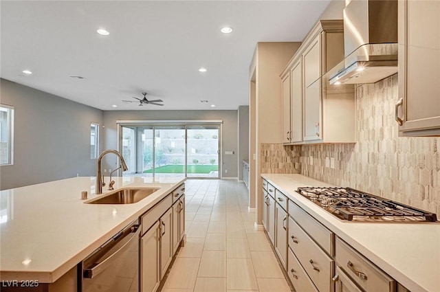 kitchen with wall chimney range hood, light countertops, decorative backsplash, stainless steel appliances, and a sink