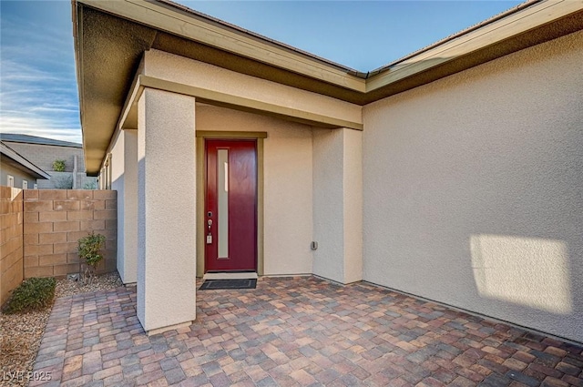 view of exterior entry with a patio area, stucco siding, and fence