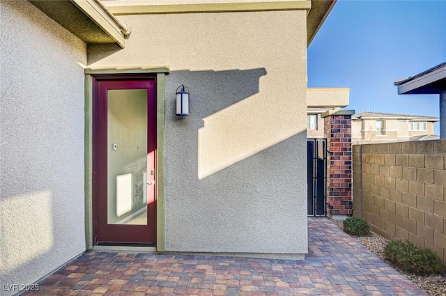 entrance to property with a gate, stucco siding, and fence