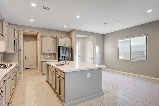 kitchen with a center island with sink, a sink, backsplash, appliances with stainless steel finishes, and light countertops