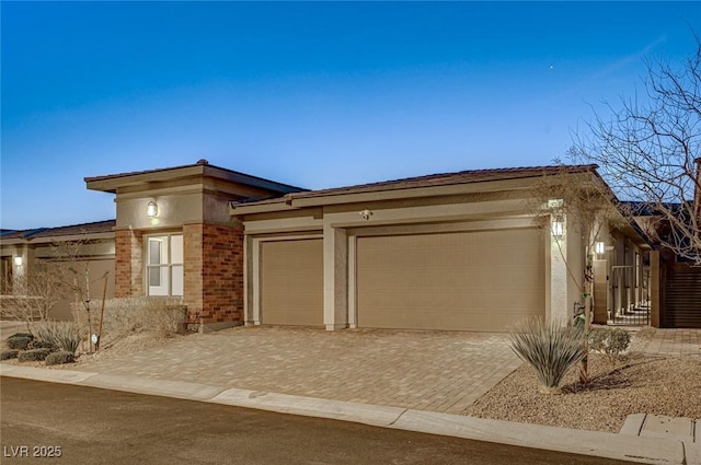 view of front of property with stucco siding, decorative driveway, brick siding, and an attached garage