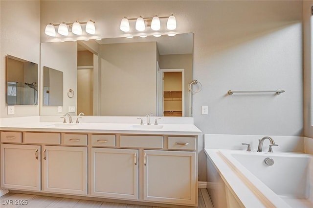 bathroom with double vanity, a tub, a walk in closet, and a sink