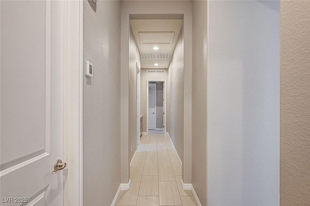 hallway with visible vents, baseboards, attic access, and a textured wall