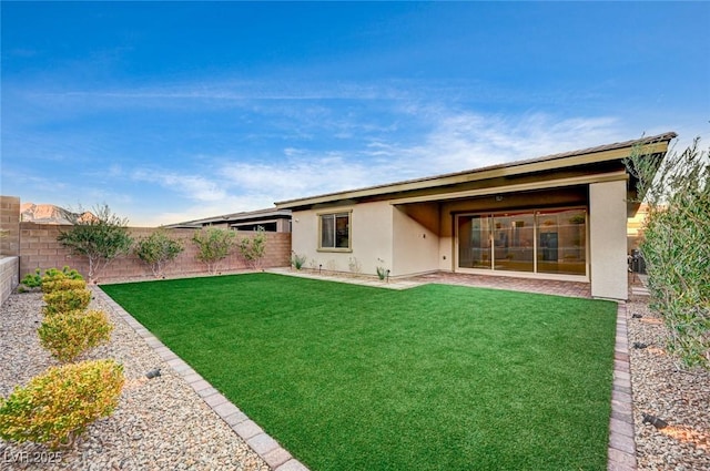 back of property with a fenced backyard, a lawn, and stucco siding