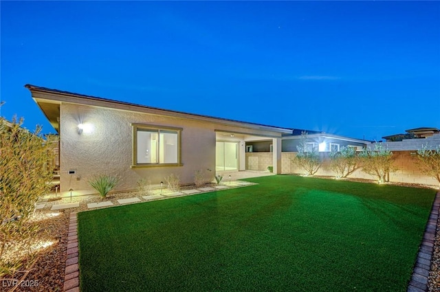 rear view of house featuring fence private yard, a lawn, and stucco siding