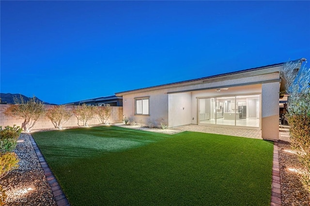 back of house featuring stucco siding, a yard, and a fenced backyard