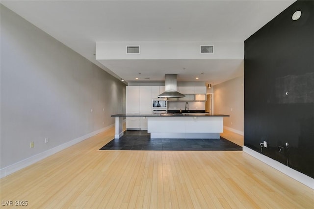 kitchen with dark countertops, stainless steel microwave, range hood, white cabinets, and a sink