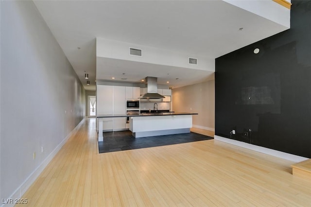 kitchen with visible vents, built in microwave, white cabinetry, dark countertops, and island range hood