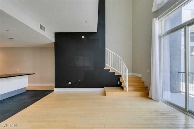 unfurnished living room with visible vents, stairway, baseboards, and wood finished floors