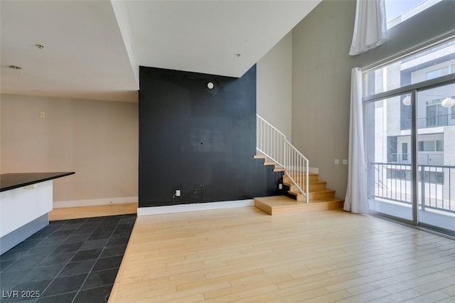 unfurnished living room with stairway, baseboards, dark wood-type flooring, and a high ceiling