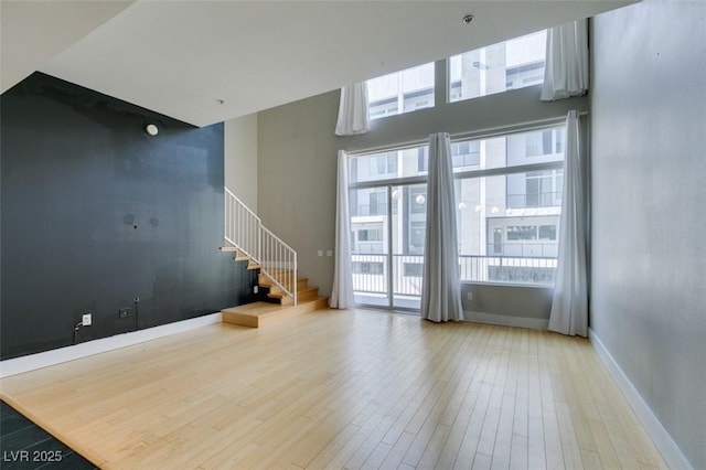 unfurnished living room featuring stairway, a towering ceiling, baseboards, and wood finished floors