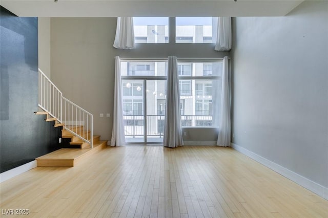 unfurnished living room with stairway, a towering ceiling, baseboards, and wood finished floors