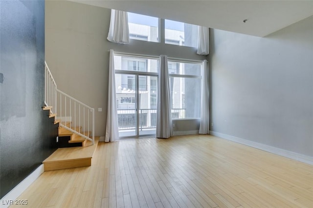 interior space featuring stairway, wood finished floors, a high ceiling, and baseboards