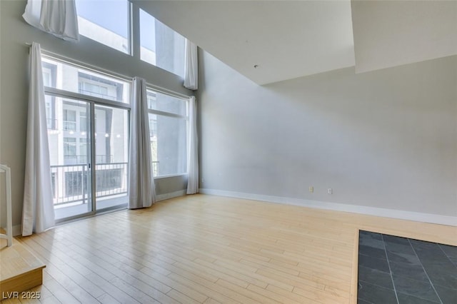 spare room with a high ceiling, wood finished floors, and baseboards