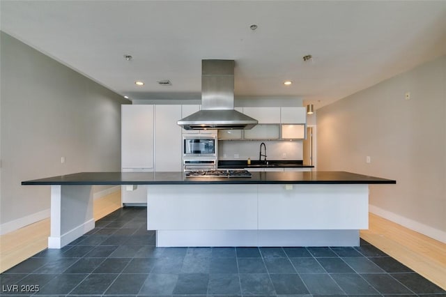 kitchen with a sink, stainless steel appliances, white cabinets, dark countertops, and island range hood