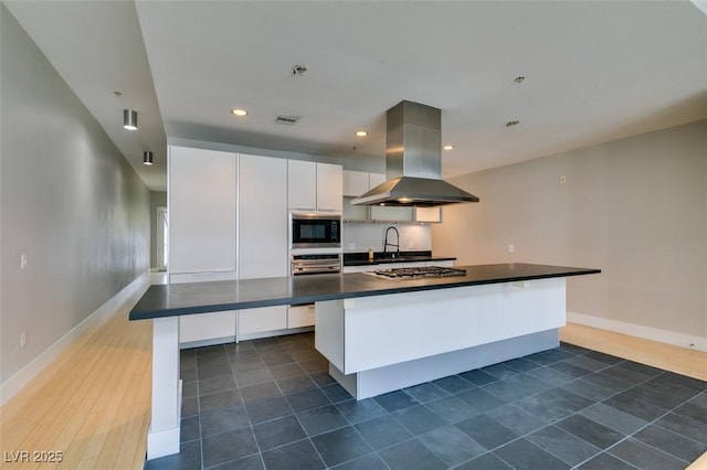 kitchen with dark countertops, visible vents, stainless steel appliances, island range hood, and white cabinetry