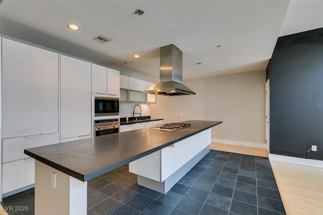 kitchen with a sink, dark countertops, appliances with stainless steel finishes, white cabinets, and island range hood