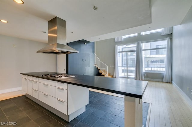 kitchen with dark countertops, stainless steel gas cooktop, island exhaust hood, white cabinets, and modern cabinets