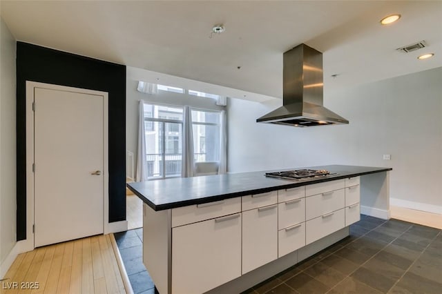 kitchen with visible vents, dark countertops, stainless steel gas stovetop, white cabinets, and island range hood