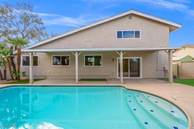 rear view of house with stucco siding, an outdoor pool, a patio, and fence