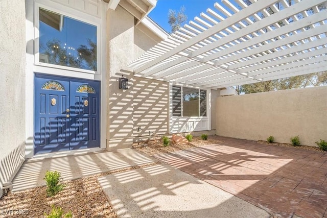 view of exterior entry featuring stucco siding and a pergola