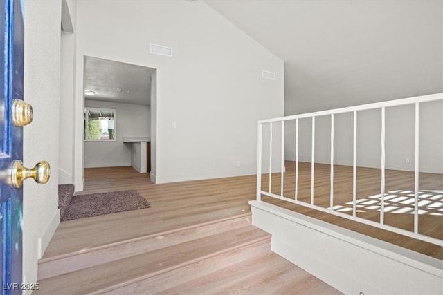 staircase featuring vaulted ceiling, visible vents, and wood finished floors