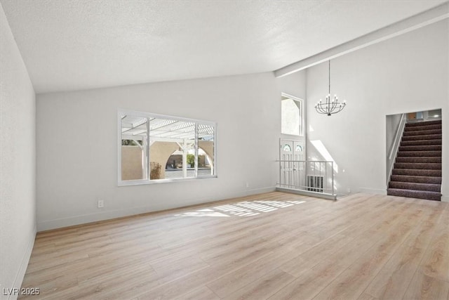 unfurnished living room with stairway, wood finished floors, baseboards, an inviting chandelier, and a textured ceiling