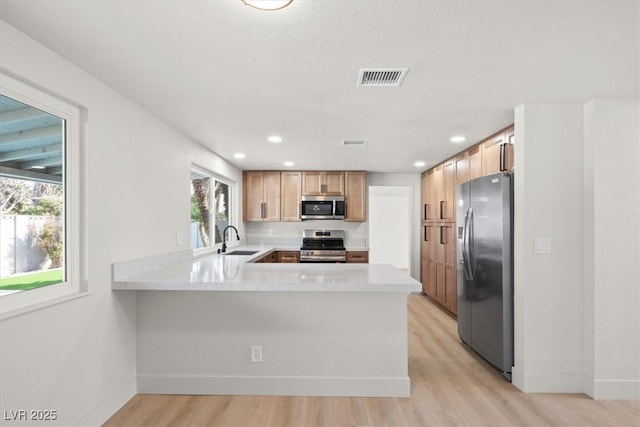 kitchen with visible vents, light countertops, a peninsula, stainless steel appliances, and a sink